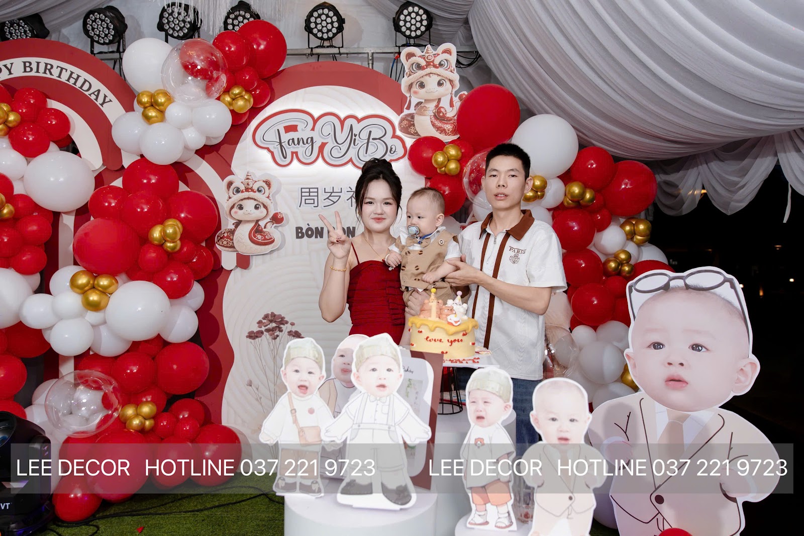Backdrop tiệc thôi nôi tông đỏ vàng kim với cổng bóng, hình chibi của bé và chữ Hán 周岁礼, thi công tại Bình Dương bởi Lee Decor 247