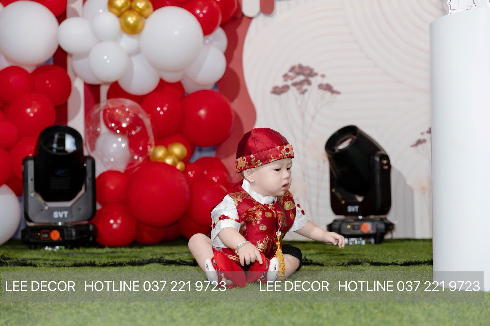 Bé mặc trang phục đỏ truyền thống ngồi trước backdrop tiệc thôi nôi phong tục người Hoa tại Bình Dương, Lee Decor 247 thi công