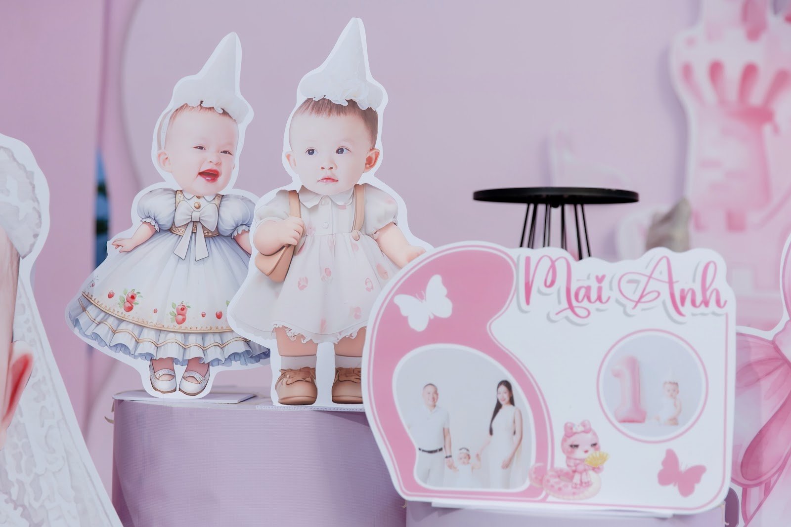 Hai hình chibi vẽ từ ảnh thật của bé gái đặt cạnh bảng thông tin thôi nôi hình nơ tông hồng