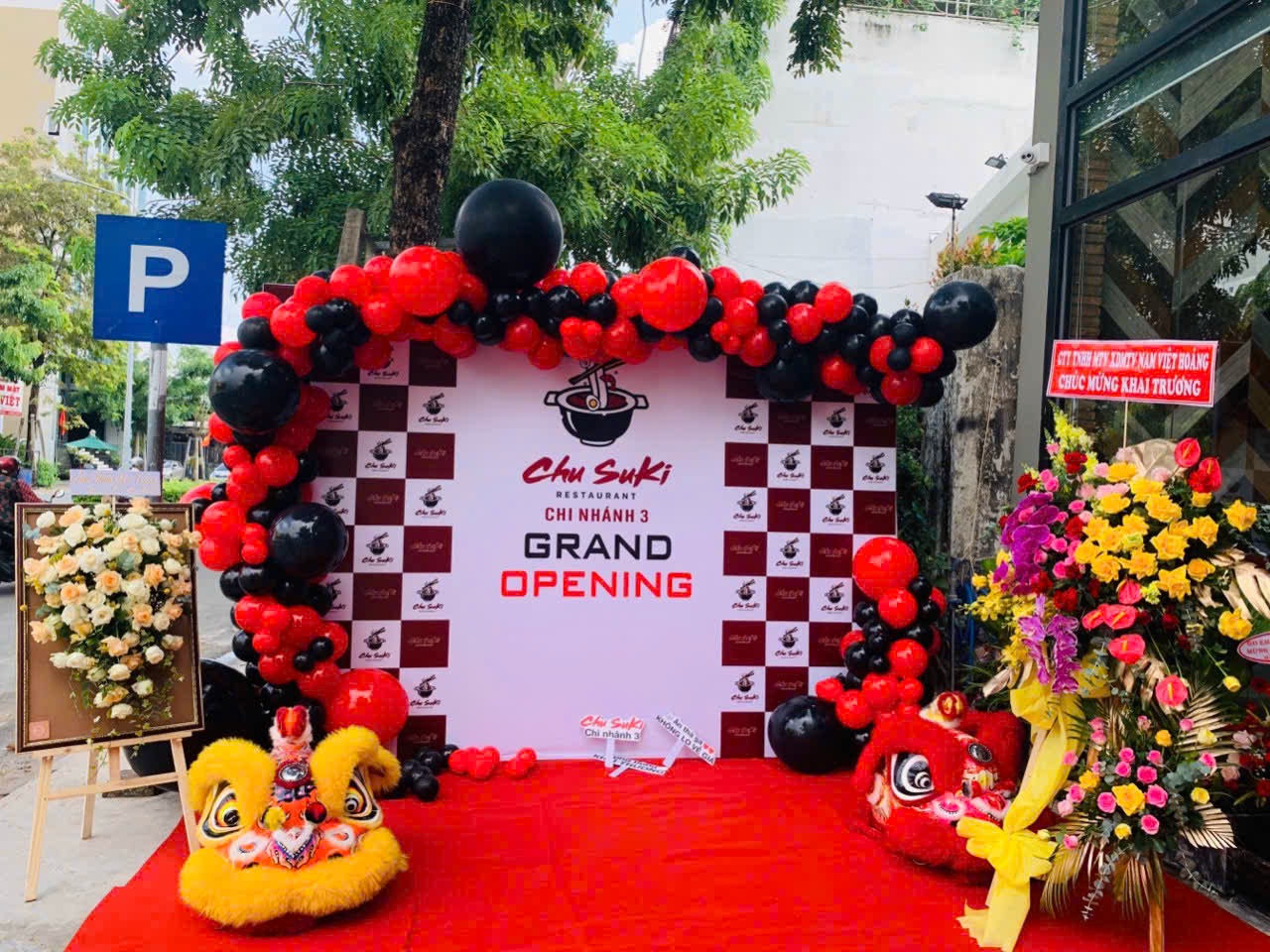 Trang trí lễ khai trương chuỗi lẩu Chusuki chi nhánh 2 tại Bình Dương — backdrop Grand Opening, cổng bóng đỏ đen, thảm đỏ và múa lân do Lee Decor 247 thi công