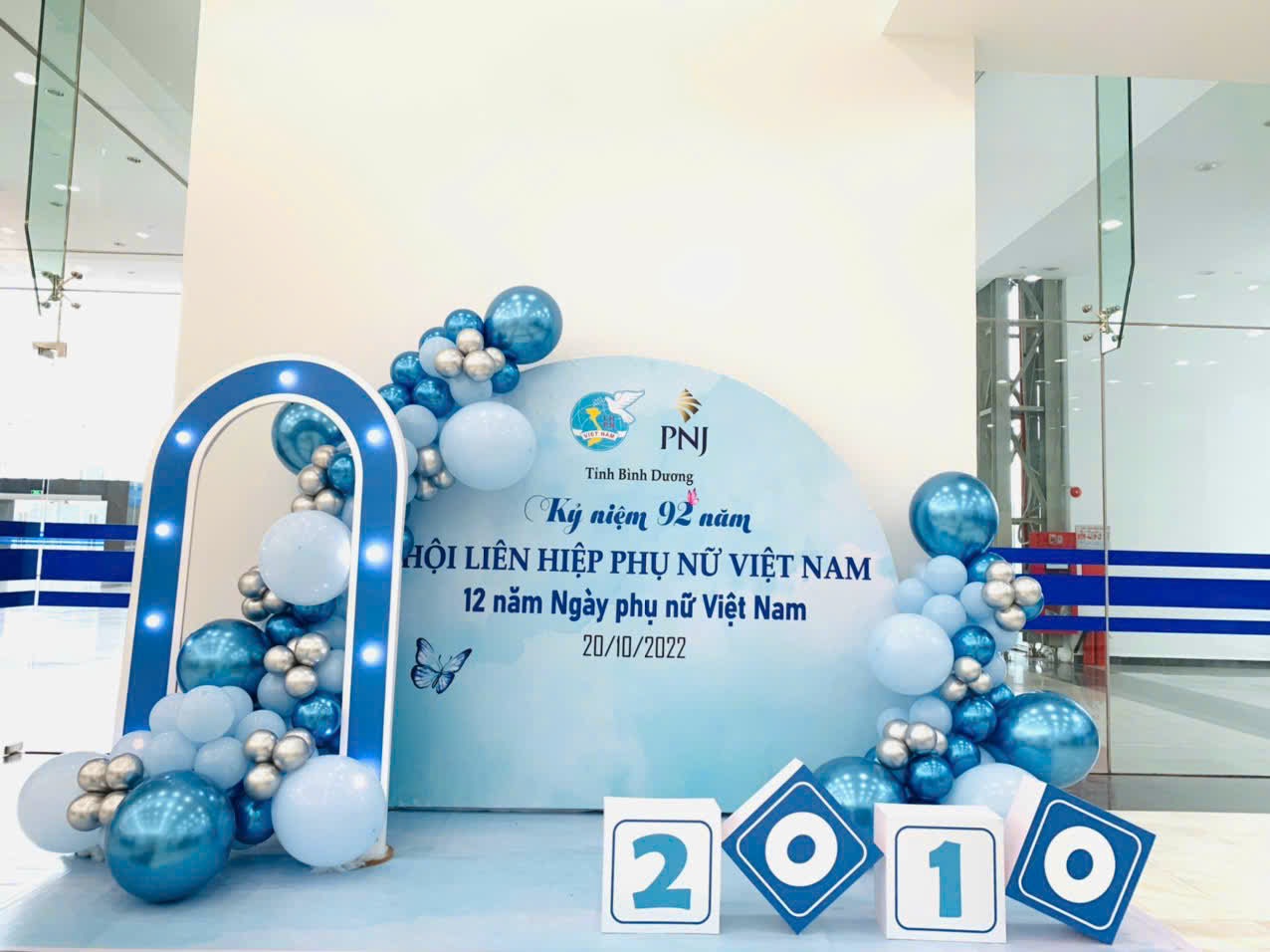 Trang trí sự kiện kỷ niệm 92 năm Hội Liên hiệp Phụ nữ Việt Nam tại PNJ Bình Dương — backdrop và cổng bóng tông xanh bạc theo nhận diện thương hiệu, Lee Decor 247 thi công