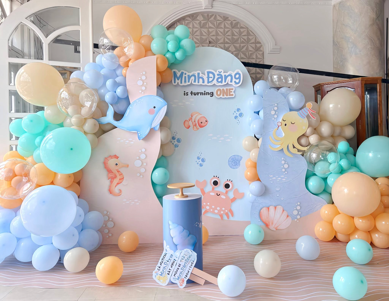 Trang trí tiệc thôi nôi cho bé concept đại dương tông xanh pastel tại Thuận An, Bình Dương — backdrop tạo hình và cột bóng do Lee Decor 247 thi công tận nơi